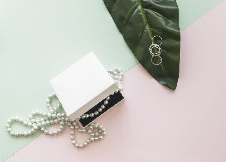 overhead-view-pearl-necklace-white-box-rings-leaf-pastel-background(1)